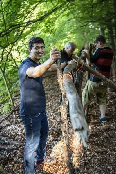Person hält einen Stock und lächelt beim Bau einer selbstgebauten Seilbrücke