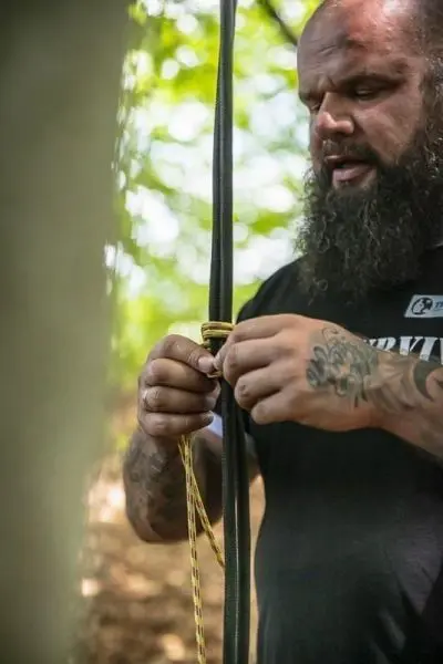 Person knotet Seil an einem Baumstamm beim Survival Training