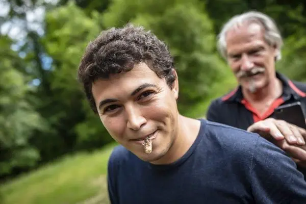 Person lächelt mit etwas im Mund, eine weitere Person im Hintergrund