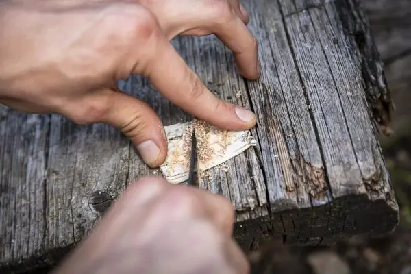 Person schneidet mit einem Messer in ein Stück Holz
