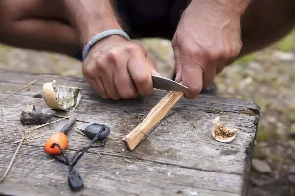 Person schnitzt mit einem Messer einen Holzstock auf einem Tisch