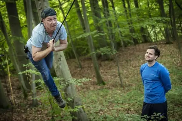 Person schwingt an Seil zwischen Bäumen, Person schaut zu
