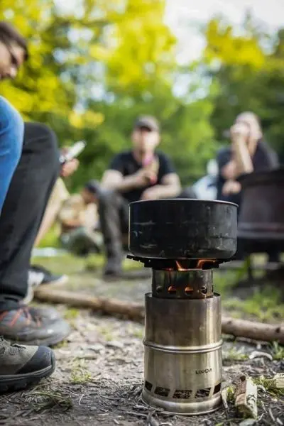 Person sitzt neben einem Kocher mit Flammen beim Kochen im Freien