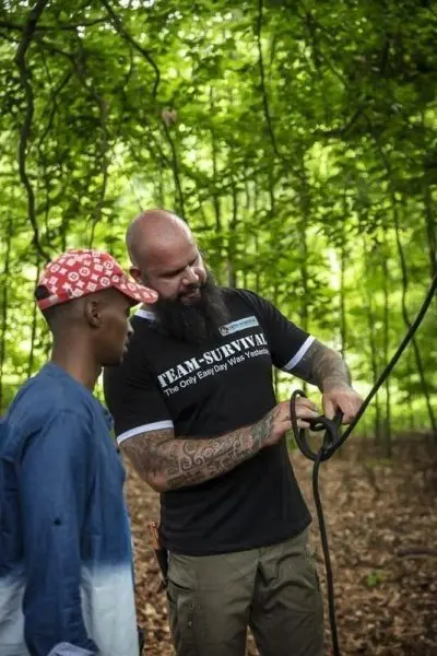 Person zeigt einer anderen Person den Umgang mit einem Seil im Wald beim Survival Training