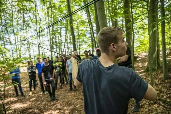 Person zieht an einem Seil in einem Wald mit Gruppe im Hintergrund