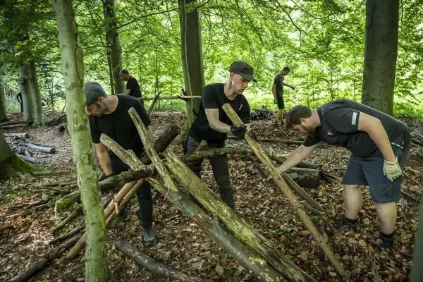 Personen bauen eine Struktur aus Ästen im Wald beim Survival Training
