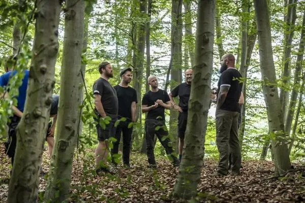 Sechs Personen stehen im Wald und diskutieren in einer Gruppe