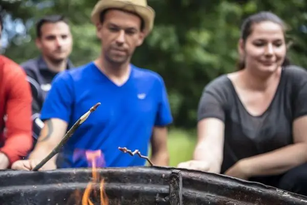 Stock mit Essen über Feuer geröstet, Teilnehmer im Hintergrund beobachten
