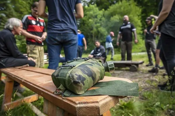 Tarnfarbene Wasserflasche liegt auf einer Holzbank beim Überlebenstraining