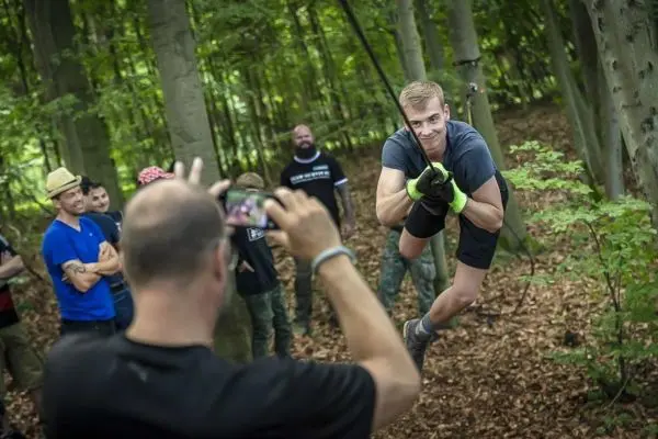 Teilnehmer schwingt an einer Seilbrücke durch den Wald, während andere zuschauen