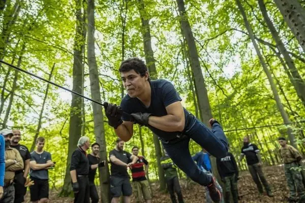 Teilnehmer überquert selbstgebaute Seilbrücke zwischen Bäumen im Wald