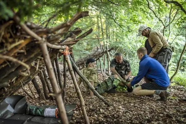 Vier Personen arbeiten an einer improvisierten Trage unter einem selbstgebauten Shelter