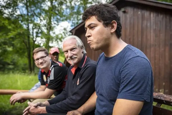 Vier Personen sitzen auf einer Bank vor einer Holzhütte im Freien