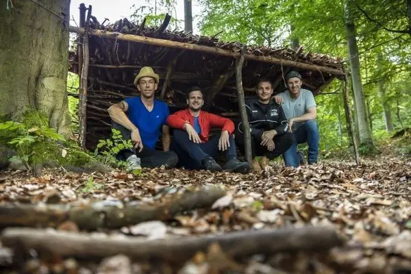 Vier Personen sitzen vor einer selbstgebauten Hütte im Wald