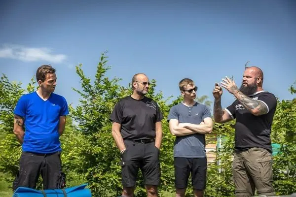 Vier Personen stehen vor einer grünen Kulisse und hören einem Redner zu