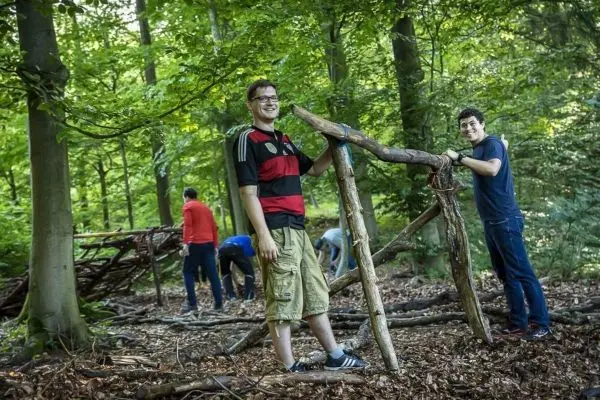 Zwei Personen bauen eine Holzkonstruktion im Wald aus Ästen und Zweigen