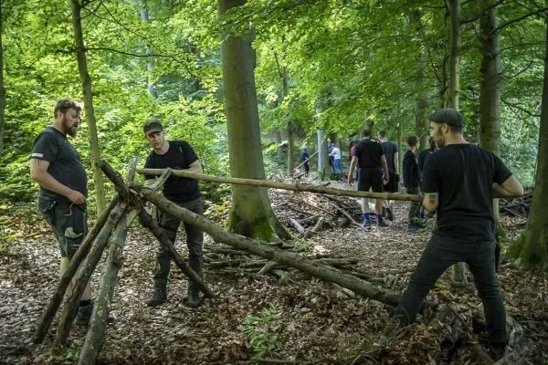 Zwei Personen bauen eine Holzstruktur aus Ästen im Wald