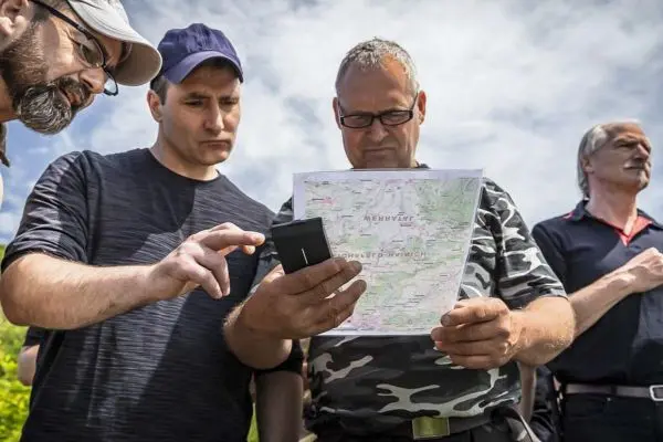 Zwei Personen betrachten eine Karte, während eine dritte Person ein Smartphone hält