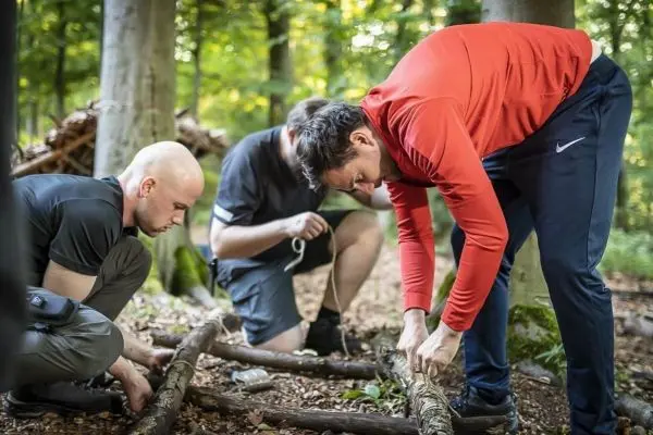 Zwei Personen binden Äste mit Schnur zu einer Konstruktion im Wald