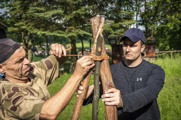 Zwei Personen binden mit Schnüren eine Holzstruktur zusammen