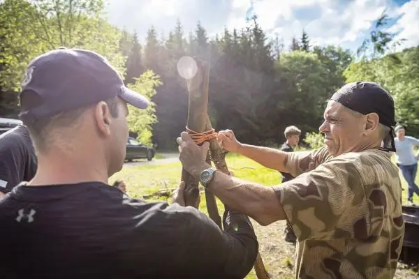 Zwei Personen binden mit Schnüren einen Stock zu einer Konstruktion zusammen