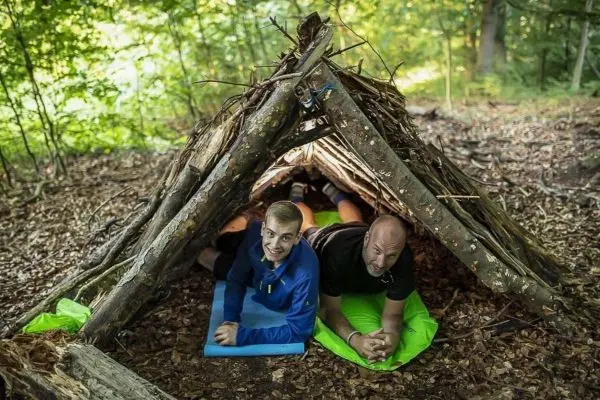 Zwei Personen liegen in einer improvisierten Tarp-Notunterkunft aus Ästen