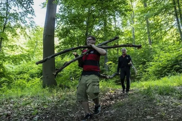 Zwei Personen tragen Äste durch einen Waldweg