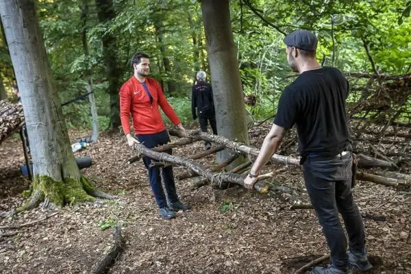 Zwei Personen tragen einen großen Ast im Wald beim Überlebenstraining
