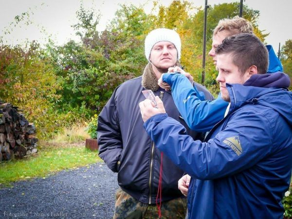 Drei Personen betrachten ein Smartphone in einer natürlichen Umgebung