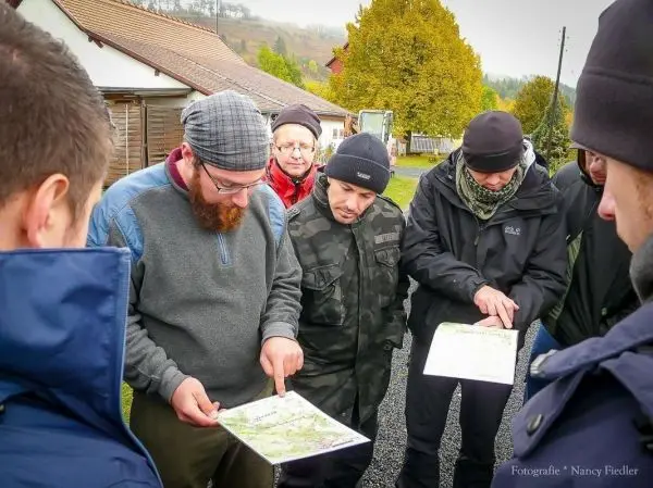 Gruppenteilnehmer betrachten Karten und diskutieren Orientierungspunkte im Freien