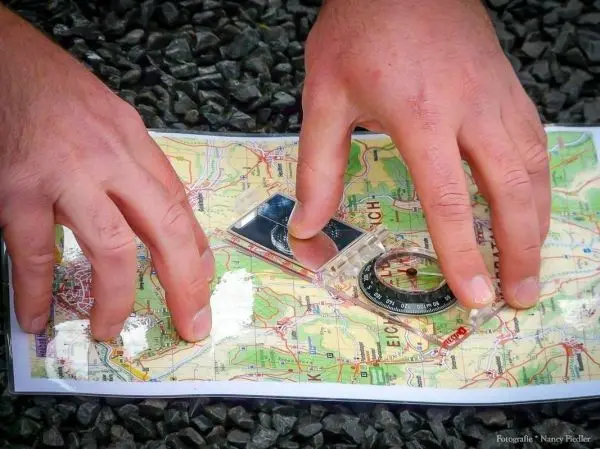 Hände legen einen Kompass auf eine Landkarte zur Orientierung