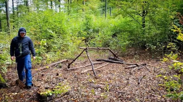 Holzkonstruktion aus Ästen steht im Wald, während jemand vorbeigeht