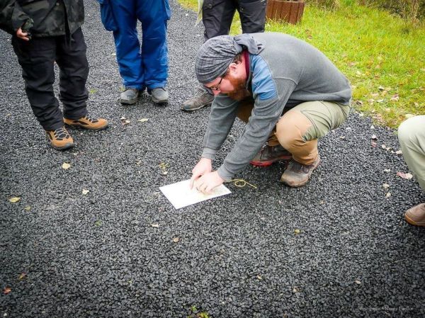 Mann kniet auf dem Boden und zeichnet mit einem Stift auf ein Blatt Papier