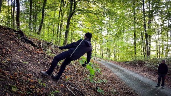 Mann nutzt Seil zur Stabilisierung beim Abstieg an einem Hang im Wald