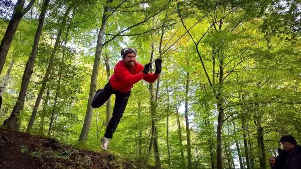 Mann springt über einen Abhang im Wald und hält eine Schnur in der Hand