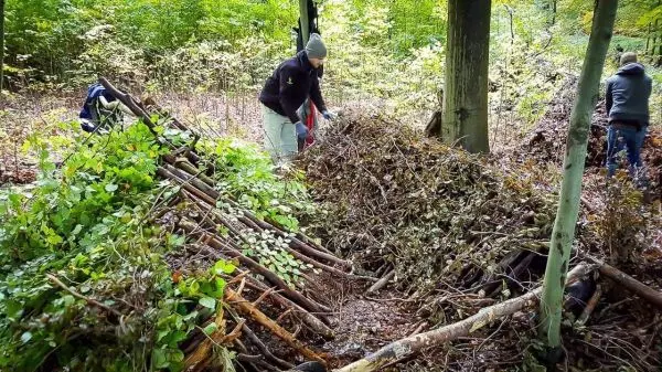 Person baut eine Struktur aus Ästen und Blättern im Wald