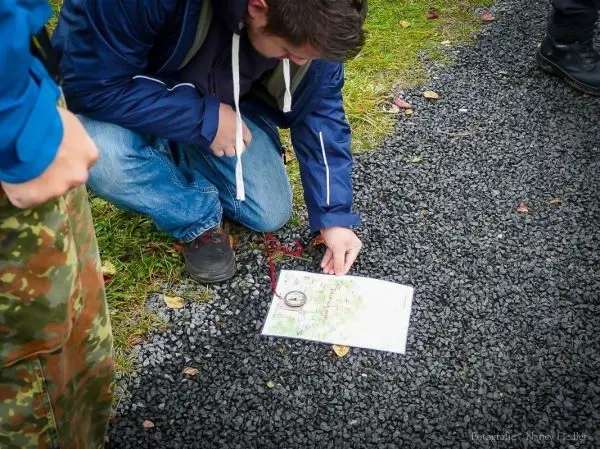 Person betrachtet Karte und Kompass auf dem Boden beim Orientieren