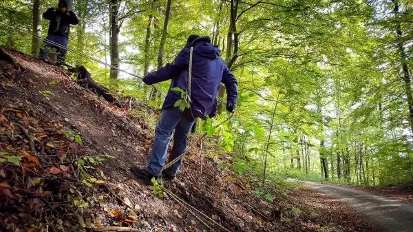 Person klettert einen steilen Hang mit Seil hinauf