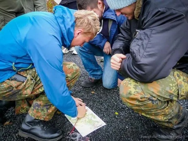 Person schaut auf eine Karte und erklärt sie anderen Personen beim Überlebenstraining