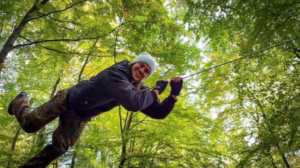 Person schwingt an einem Seil zwischen Bäumen im Wald