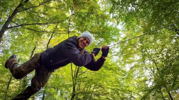 Person schwingt an einem Seil zwischen Bäumen im Wald