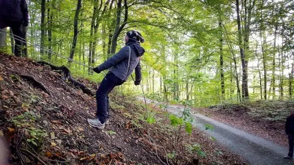 Person sichert sich mit Seil beim Abseilen an einem Hang im Wald