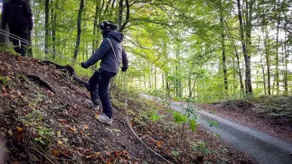 Person sichert sich mit Seil beim Abstieg an einem Hang im Wald
