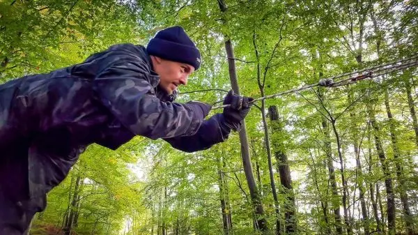 Person spannt eine Schnur zwischen Bäumen im Wald