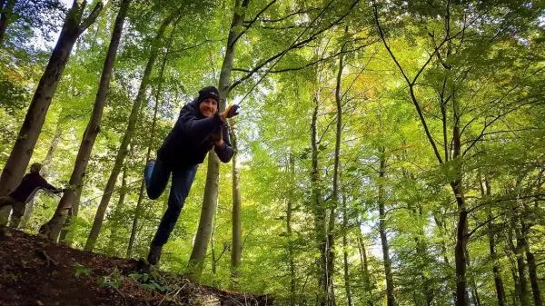 Person springt über einen Abhang im Wald und hält sich an einem Ast fest