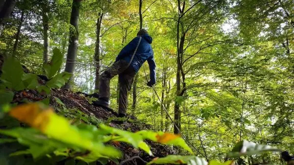 Person steht an einem Hang und hält ein Seil
