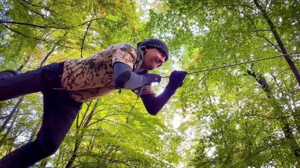 Person zieht an einer Schnur zwischen Bäumen im Wald