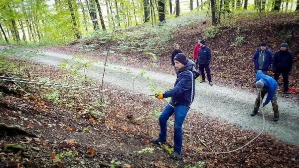 Seil wird von einer Person an einem Hang gespannt, während andere zuschauen