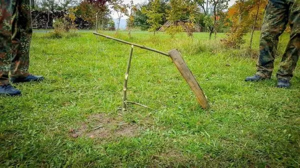 Selbstgebaute Schlingenfalle aus Holz und Schnüren im Gras