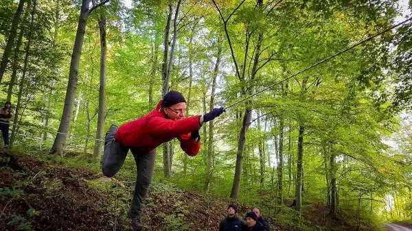 Teilnehmer nutzt Seil für eine selbstgebaute Seilbrücke im Wald